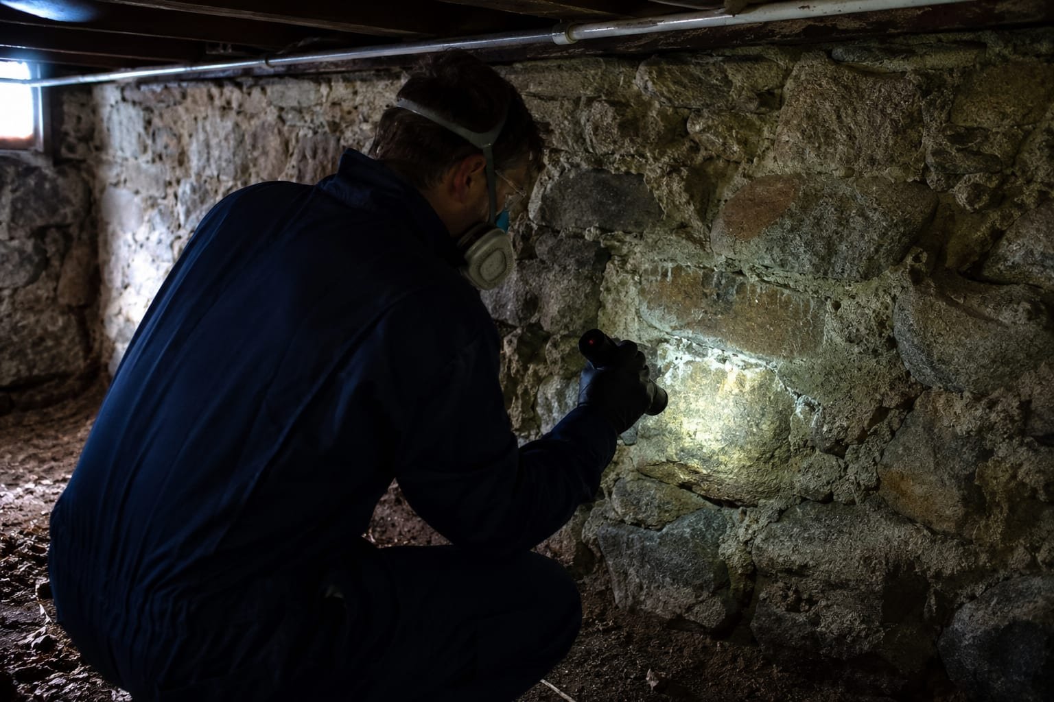 Technician examining a damp fieldstone foundation in an old mill village house in Millbury, MA